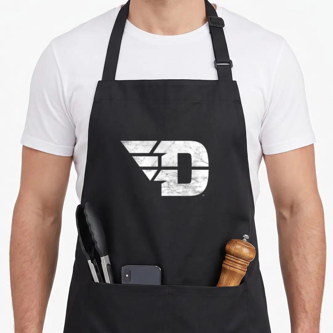 Dayton distressed apron - Large white distressed letter D with wing shapes extending left — shown on a black cotton canvas apron against a white background