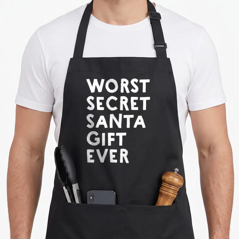 Worst elephant print apron - White stacked text reading WORST SECRET SANTA GIFT EVER — shown on a black cotton canvas apron against a white background