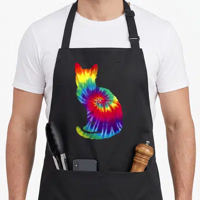 Tie kitten apron - Rainbow tie-dye cat silhouette print in red yellow green blue purple — shown on a black cotton canvas apron against a white background