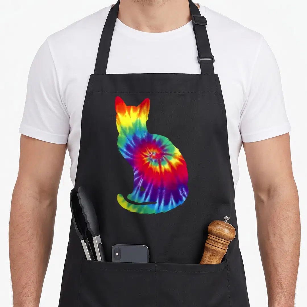 Tie kitten apron - Rainbow tie-dye cat silhouette print in red yellow green blue purple — shown on a black cotton canvas apron against a white background