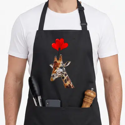 Funny giraffe animal apron - Watercolor giraffe head holding four red heart balloons on black strings — shown on a black cotton canvas apron against a white background