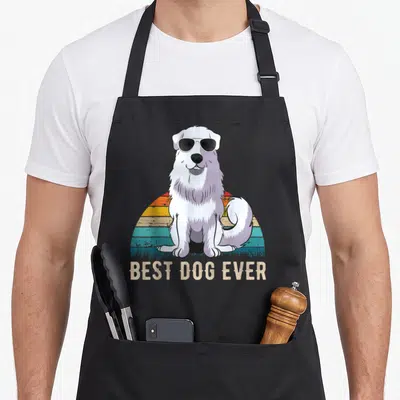 Pyrenean dog apron - White dog wearing sunglasses sitting before striped sun with BEST DOG EVER text below — shown on a black cotton canvas apron against a white background