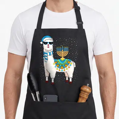 Menorah hanukkah apron - Cartoon llama with blue hat scarf and gold menorah on back amidst white snow dots — shown on a black cotton canvas apron against a white background