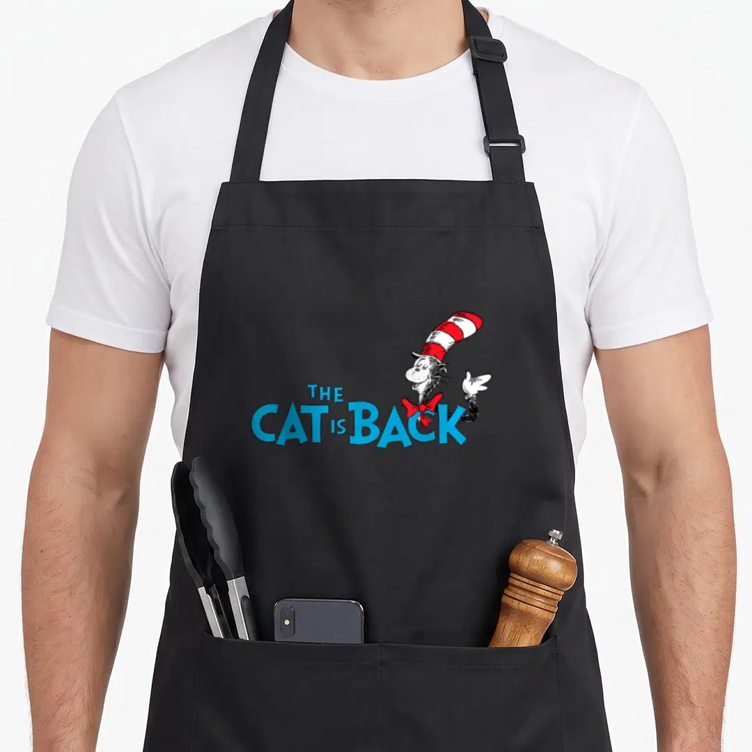General cat apron for women - Cartoon cat with red white striped hat next to blue stacked text reading THE CAT IS BACK — shown on a black cotton canvas apron against a white background