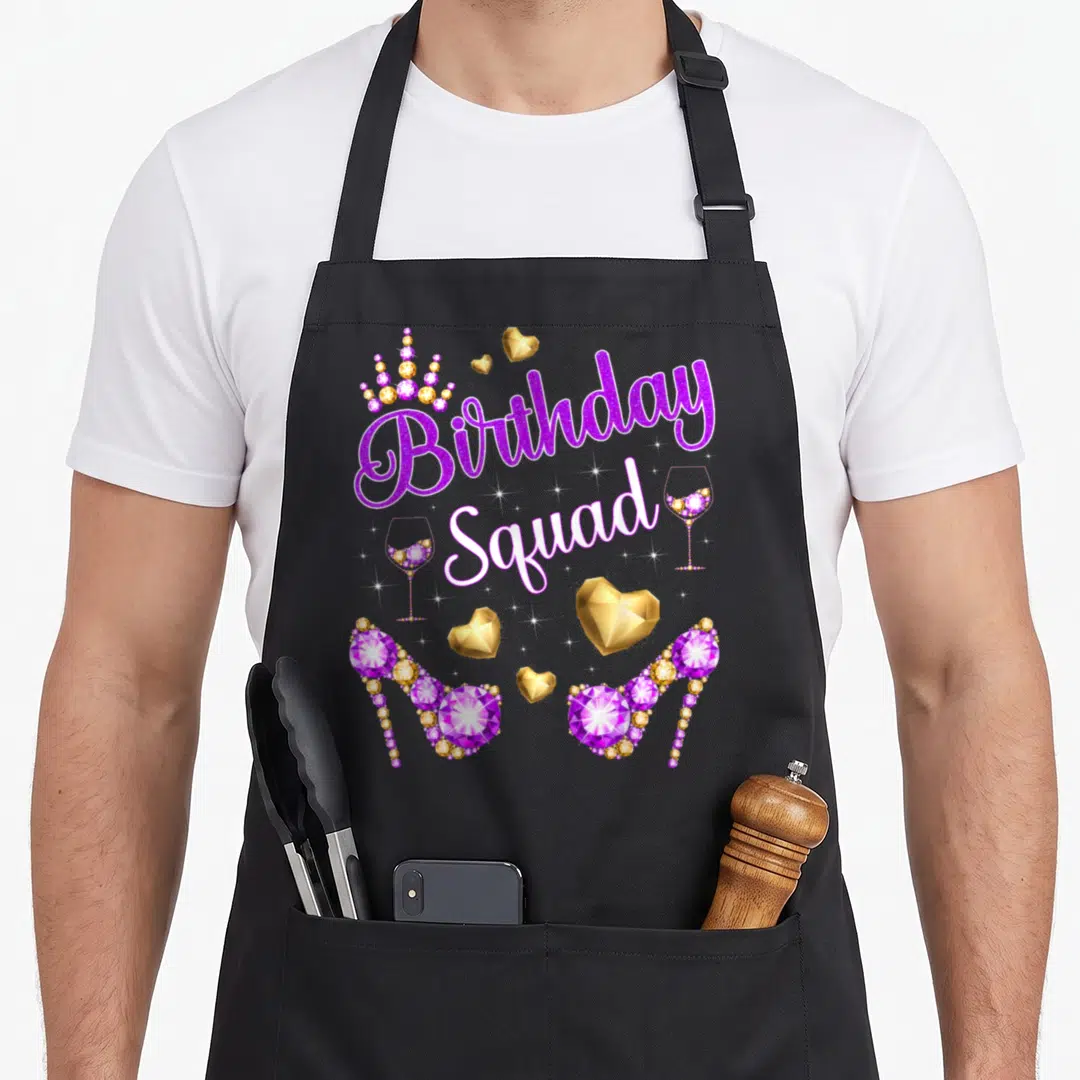 Squad heel birthday apron - Purple Birthday Squad text with jeweled heels and crowns — shown on a black cotton canvas apron against a white background