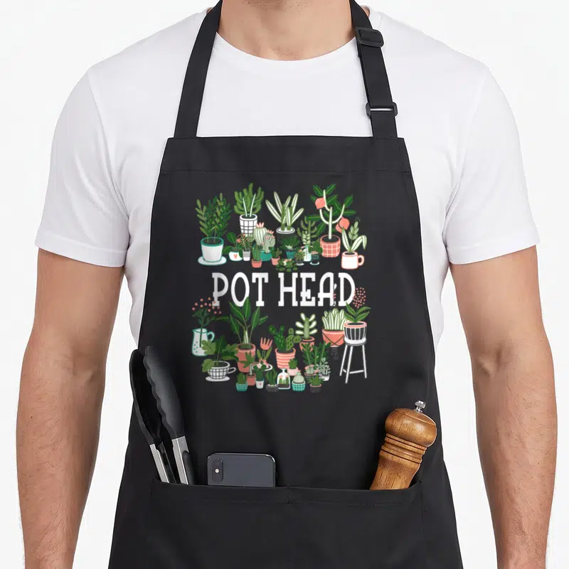 Plant gardener apron - POT HEAD text surrounded by cartoon potted plants in green white red and black — shown on a black cotton canvas apron against a white background