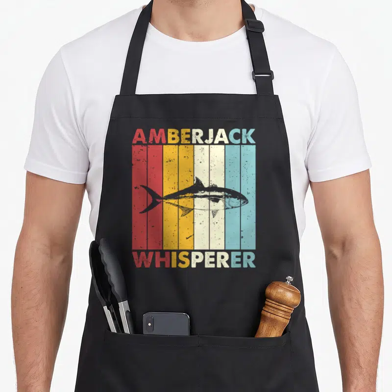 Amberjack fish apron - Grey amberjack fish over red orange yellow cream and blue vertical stripes with matching text — shown on a black cotton canvas apron against a white background