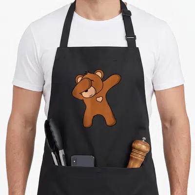 Dab teddy bear apron - Brown cartoon bear dabbing with a small white heart on its chest — shown on a black cotton canvas apron against a white background