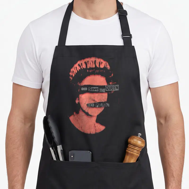 Pistol queen apron - Red halftone portrait with GOD SAVE THE QUEEN across eyes and SEX PISTOLS across mouth — shown on a black cotton canvas apron against a white background