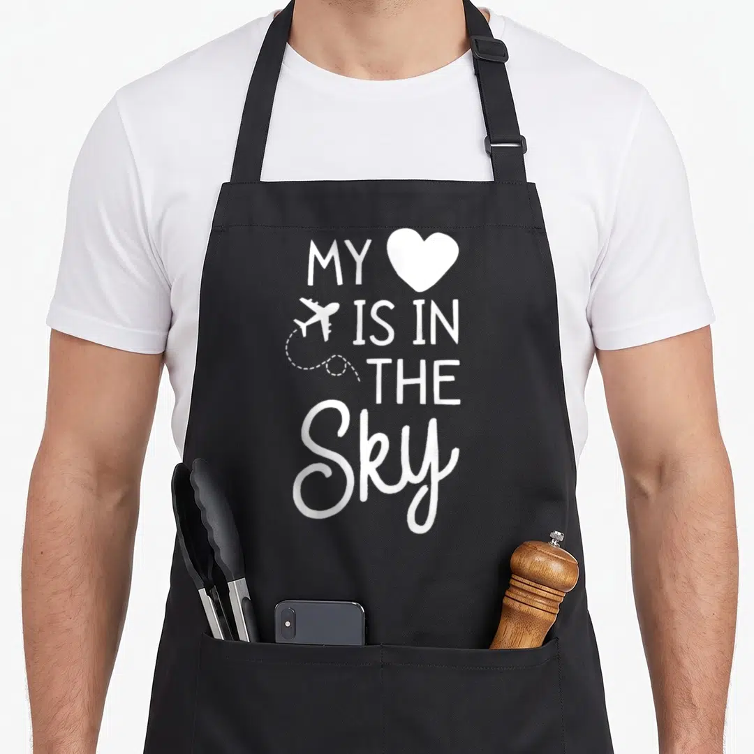 Flight sky apron - White text MY IS IN THE SKY with heart and airplane icon, vertical stack layout — shown on a black cotton canvas apron against a white background
