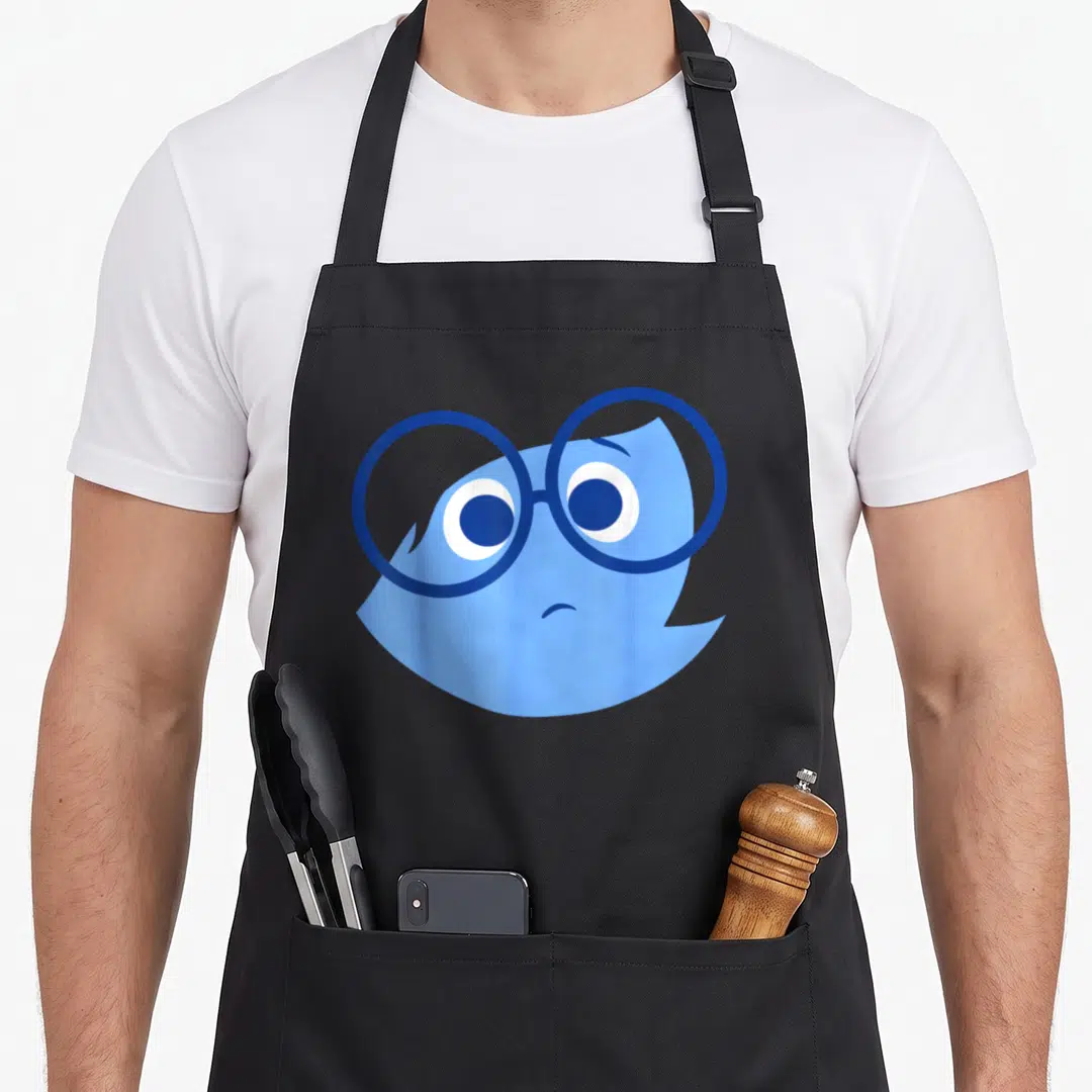 Sad halloween apron - Light blue cartoon bird head wearing a pair of dark blue round glasses — shown on a black cotton canvas apron against a white background