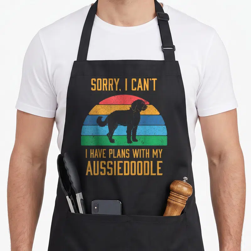 Aussiedoodle dog apron - Retro rainbow sunset with grey dog silhouette and orange text reading sorry i can't i have — shown on a black cotton canvas apron against a white background