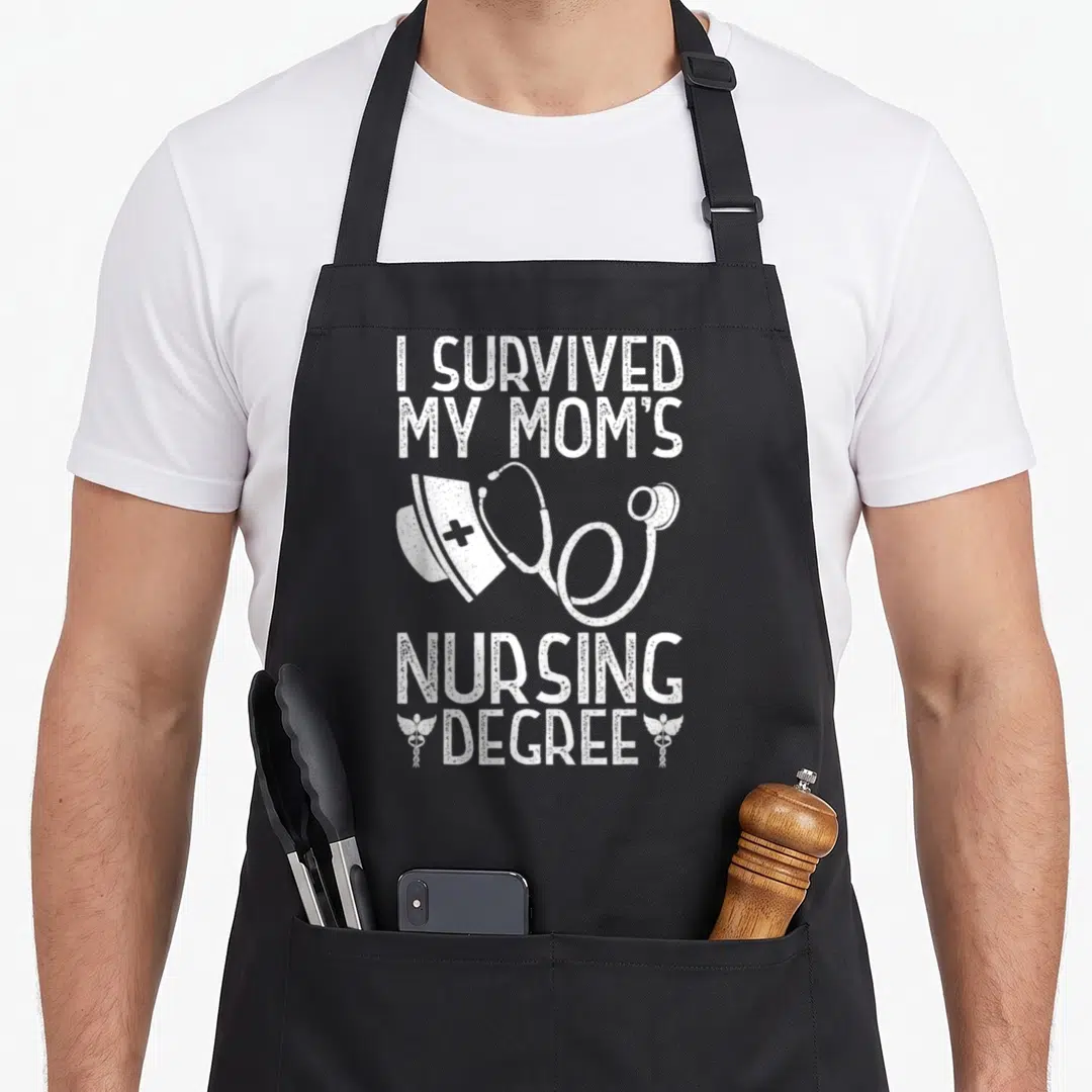 Survived nursing aprons - White distressed text I Survived My Moms Nursing Degree with nurse cap stethoscope — shown on a black cotton canvas apron against a white background