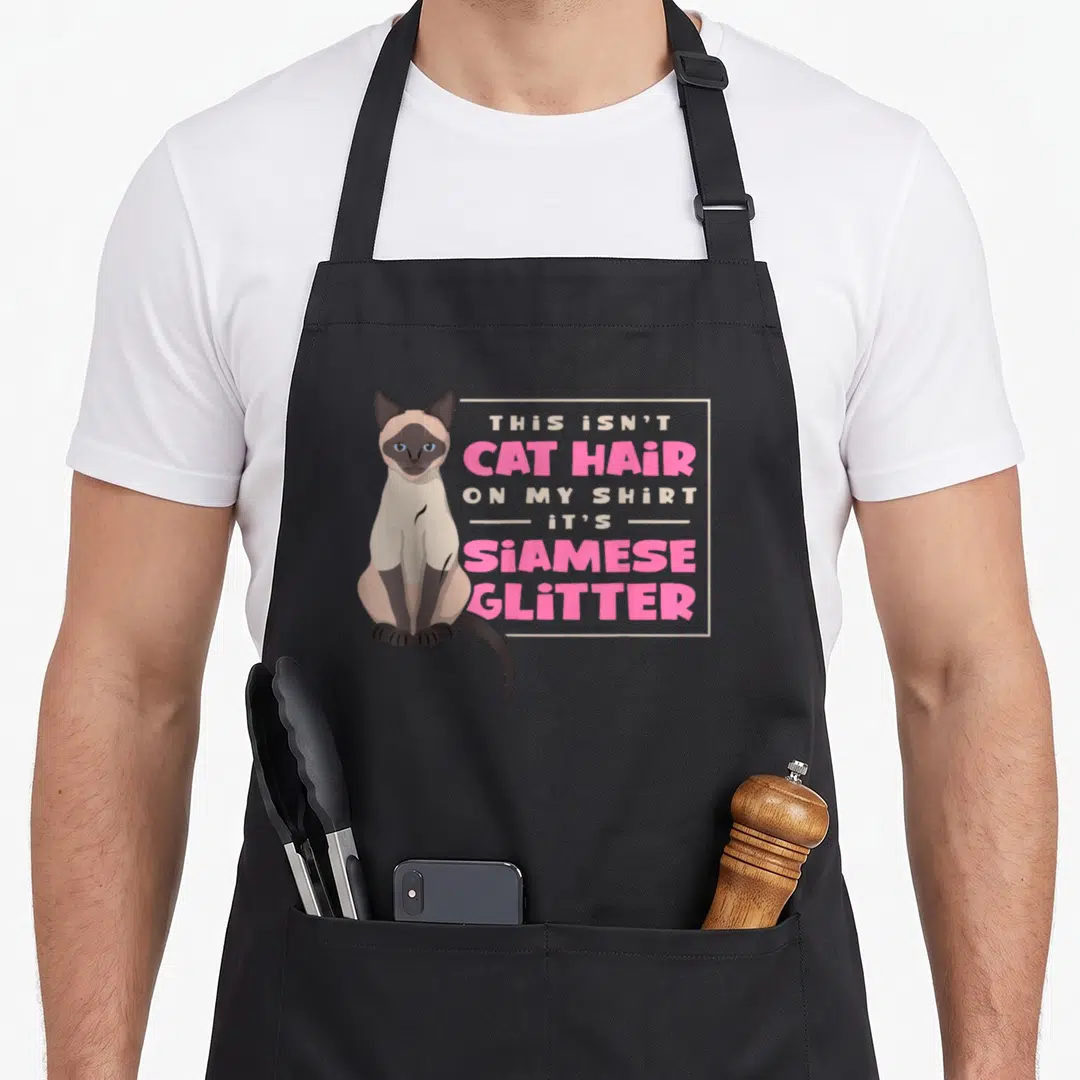 Siamese sweet cat aprons - Cartoon Siamese cat beside pink and white text reading This Isn't Cat Hair Its Siamese — shown on a black cotton canvas apron against a white background
