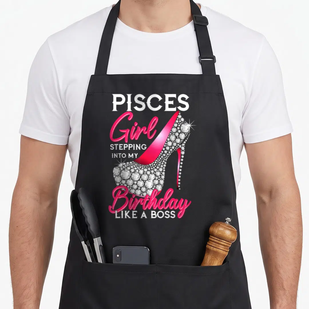 Pisce bbq boss apron - Pink rhinestone high heel shoe with Pisces birthday text — shown on a black cotton canvas apron against a white background