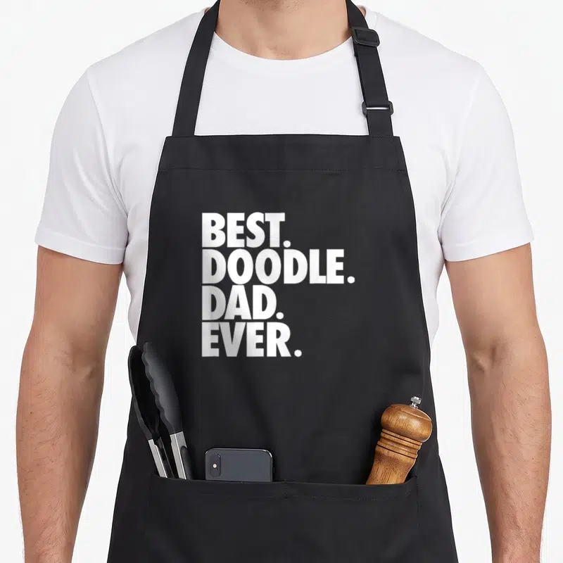 Retro doodle goldendoodle apron - White stacked text reading BEST. DOODLE. DAD. EVER. in bold block letters — shown on a black cotton canvas apron against a white background