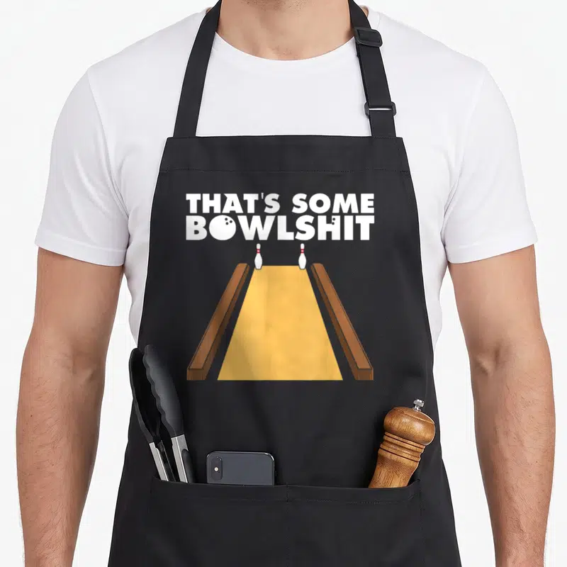 Bowlshit bowling apron - Stacked text That's Some Bowlshit with ball in O above yellow lane and two pins — shown on a black cotton canvas apron against a white background