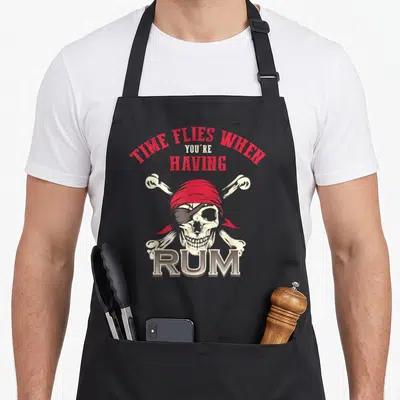 Fly wings lover apron - Distressed skull with red bandana and eye patch under arched text reading TIME FLIES WHEN — shown on a black cotton canvas apron against a white background
