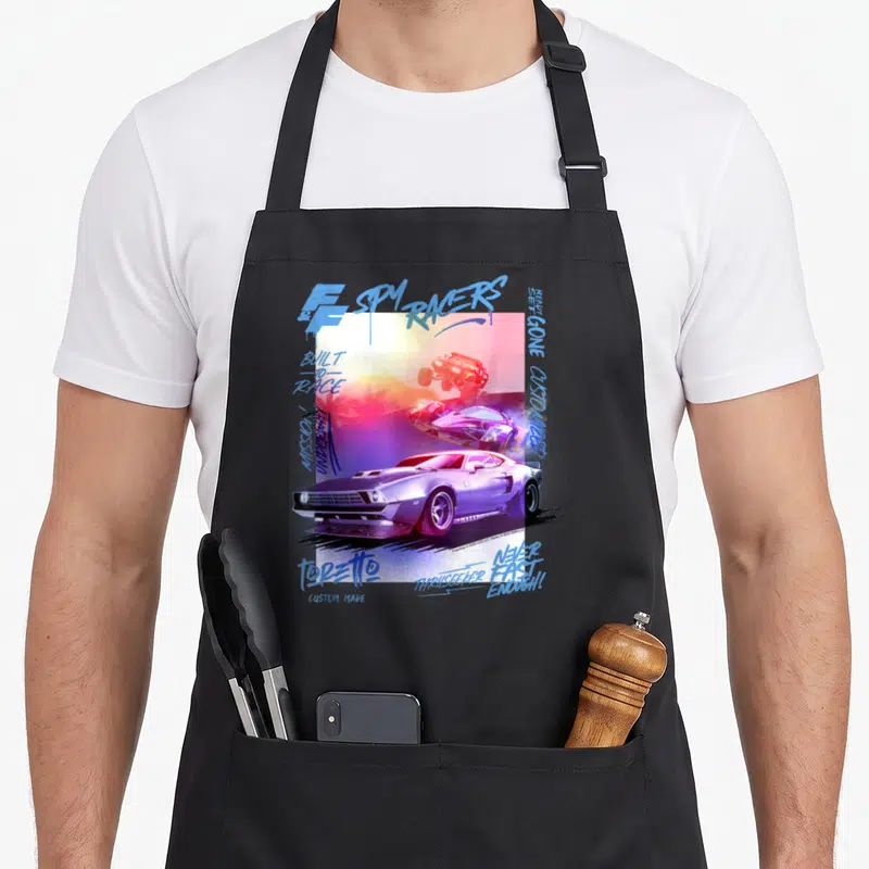 Fast racer girl apron - Three retro cars in purple and orange with SPY RACERS and BUILT TO RACE graffiti text — shown on a black cotton canvas apron against a white background