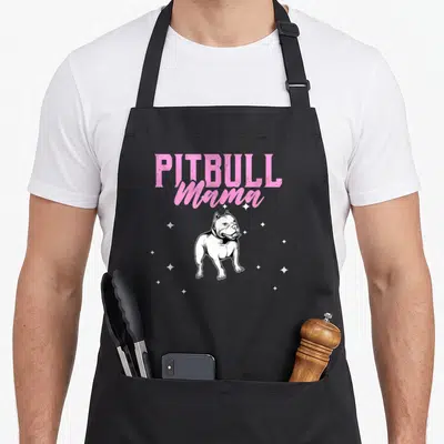 Comical dog apron - Pink PITBULL Mama text above a cartoon pitbull illustration surrounded by white stars — shown on a black cotton canvas apron against a white background