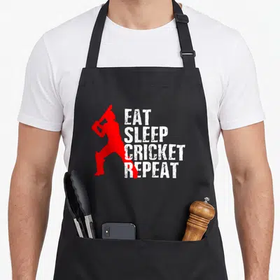 Funny player cricket apron - Red cricketer silhouette holding bat next to white stacked text EAT SLEEP CRICKET REPEAT — shown on a black cotton canvas apron against a white background