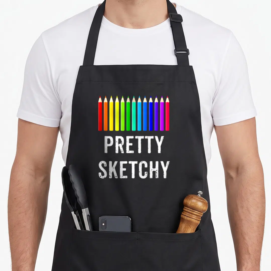 Colored pretty apron - Row of twelve colored pencils above white text reading PRETTY SKETCHY — shown on a black cotton canvas apron against a white background