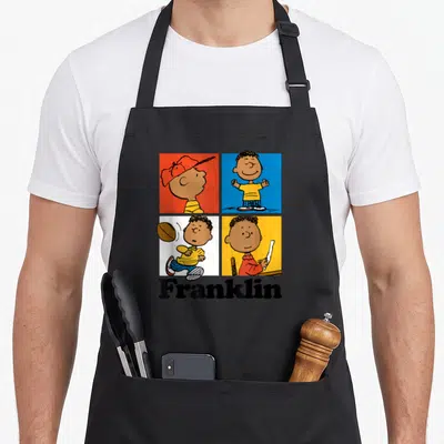 Franklin blue apron - Four colored squares with character poses above bold Franklin text — shown on a black cotton canvas apron against a white background