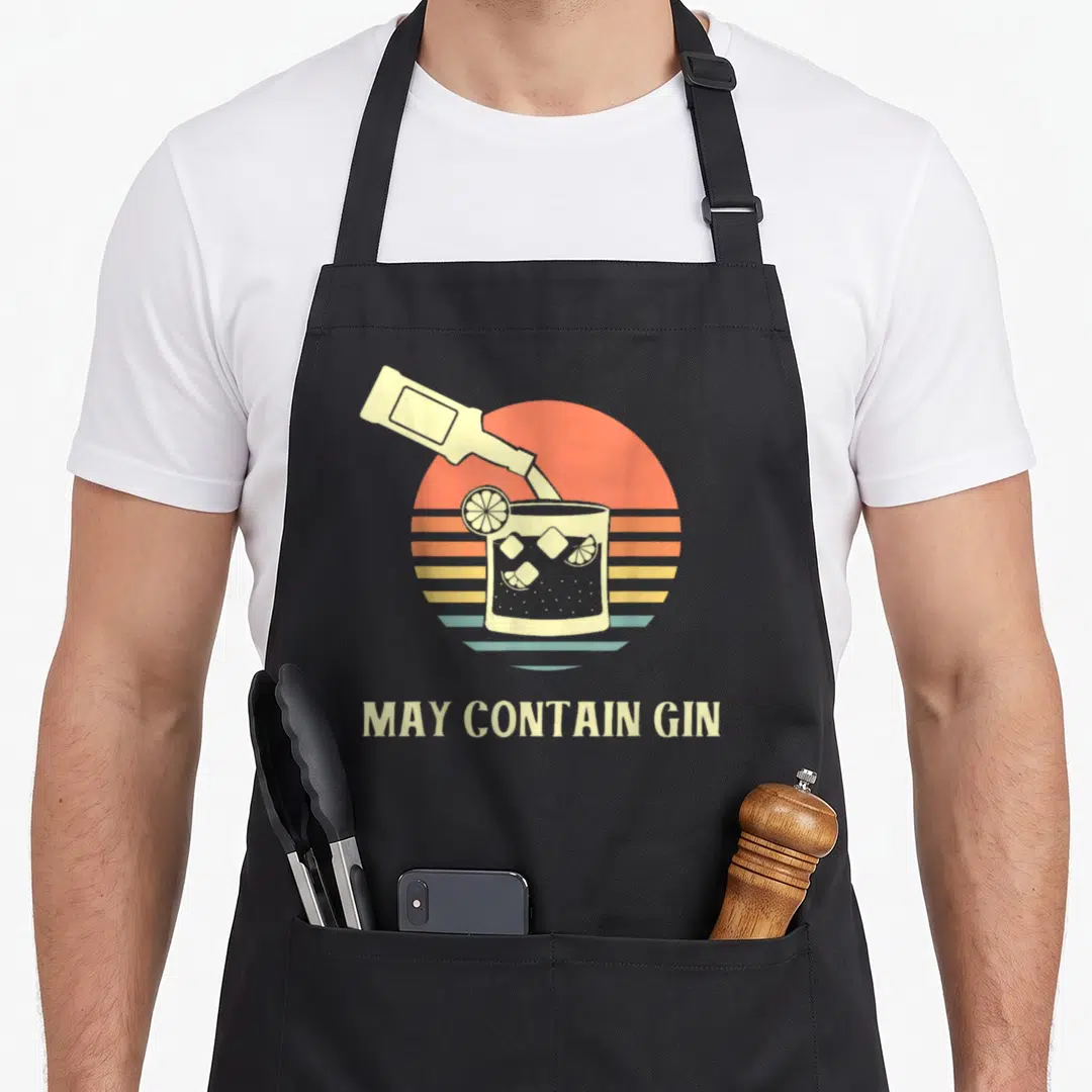 May funny gin apron - Retro bottle pouring into glass with ice and lemon slice over striped sun with text below — shown on a black cotton canvas apron against a white background