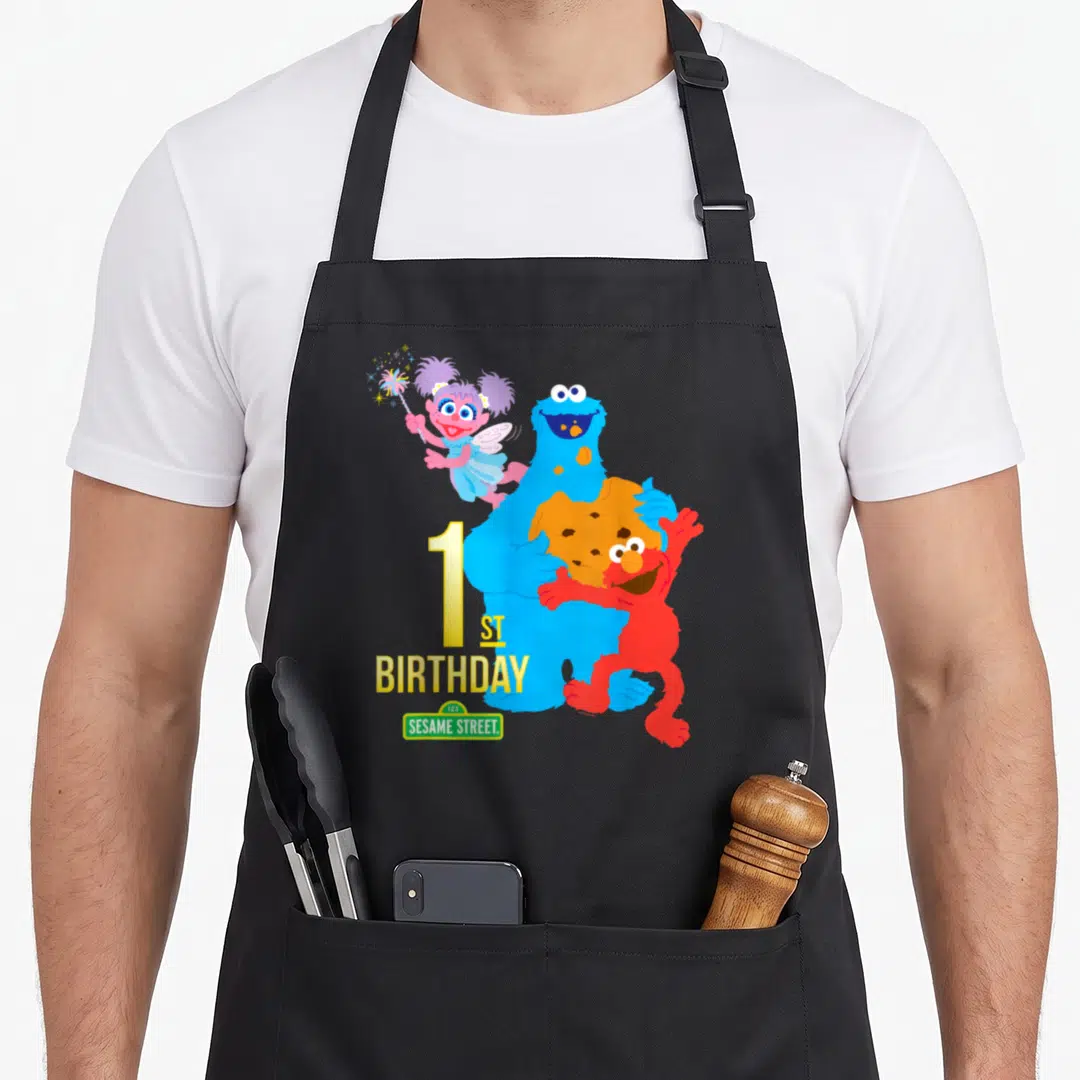 1st birthday apron - Cookie Monster holding cookie with Elmo and Abby near 1 ST BIRTHDAY text — shown on a black cotton canvas apron against a white background