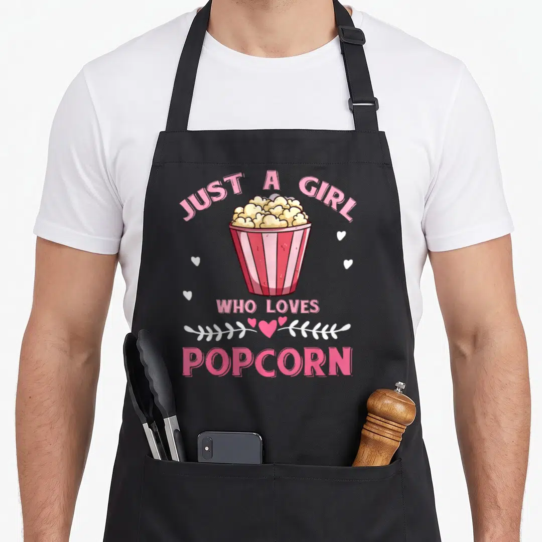 Cool popcorn apron - Pink striped popcorn bucket with Just A Girl Who Loves Popcorn text and hearts — shown on a black cotton canvas apron against a white background