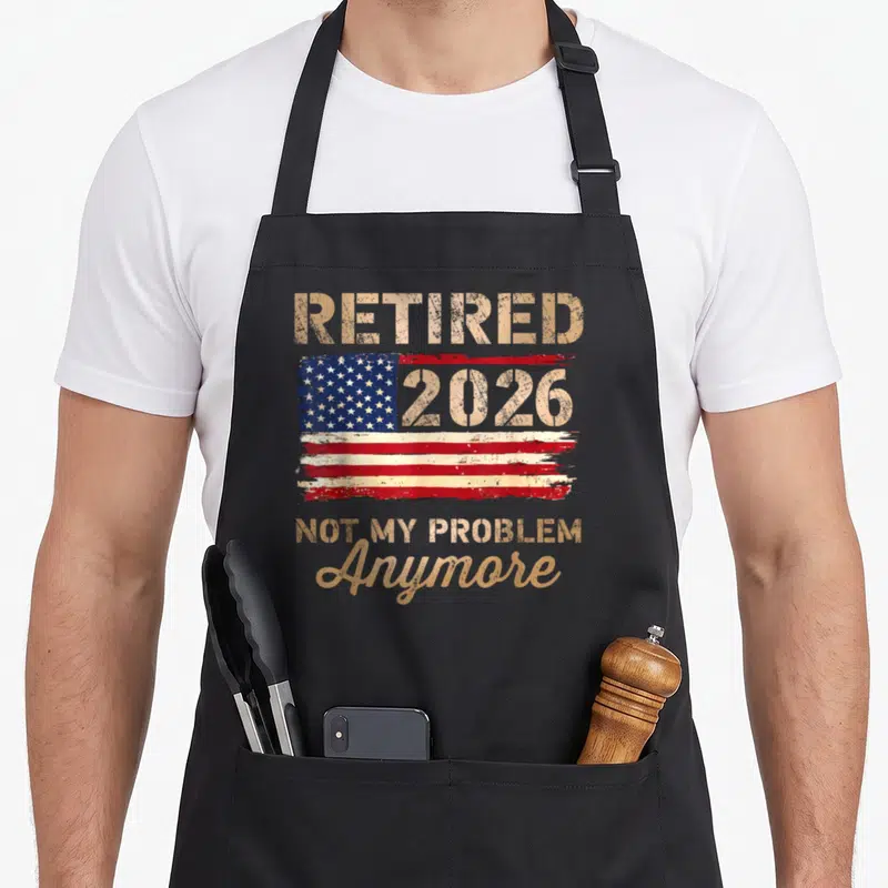 Anymore flag retirement apron - Distressed USA flag with Retired 2026 Not My Problem Anymore text in gold and red — shown on a black cotton canvas apron against a white background