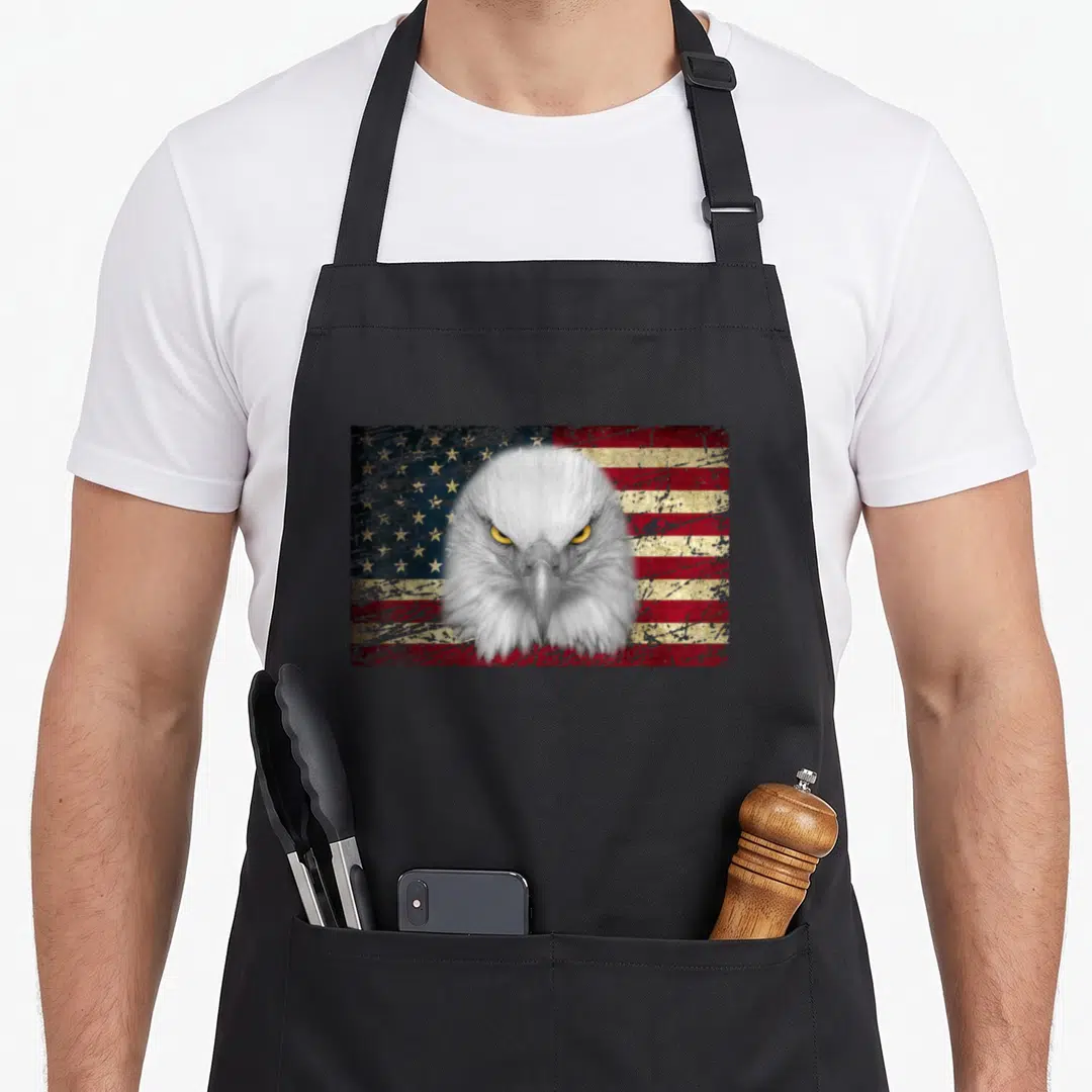 Bald american flag apron - Realistic bald eagle head over distressed red white blue and yellow USA flag — shown on a black cotton canvas apron against a white background