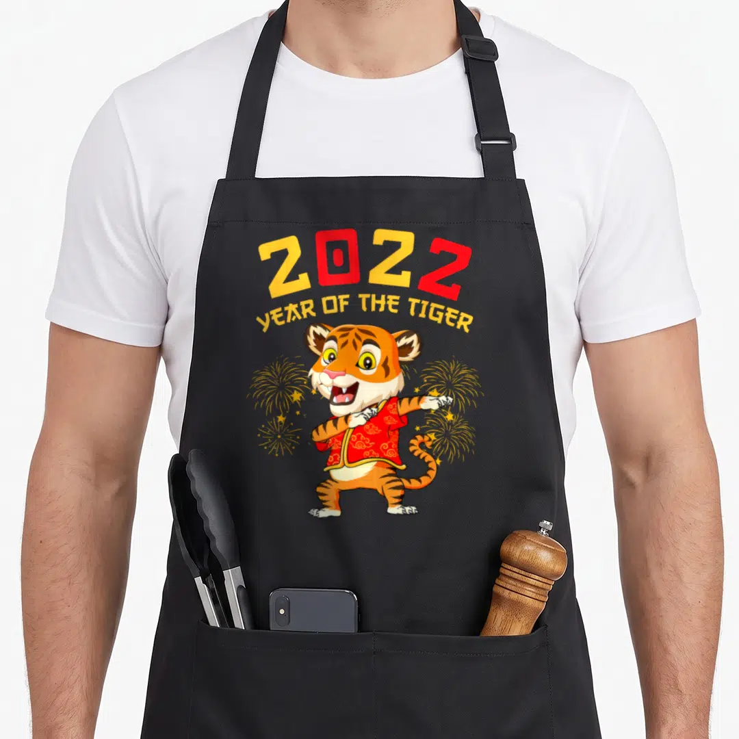 Dabbing year of the tiger apron - Cartoon tiger dabbing in red outfit under 2022 YEAR OF THE TIGER text — shown on a black cotton canvas apron against a white background