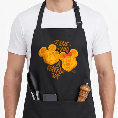 Waffle valentine's day apron - Two waffle characters with strawberry ears and arching text I LOVE YOU A WAFFLE LOT — shown on a black cotton canvas apron against a white background