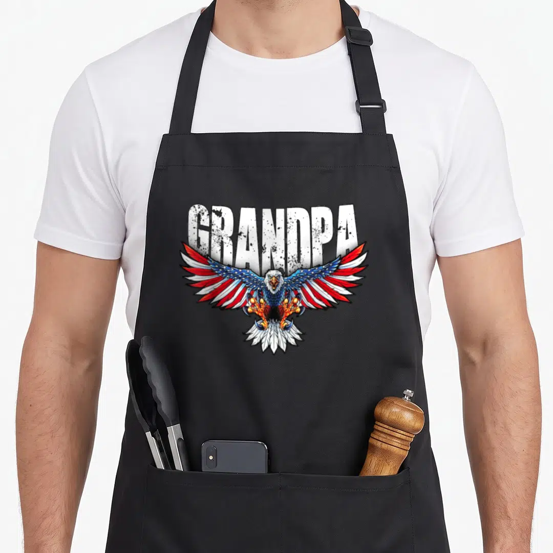 Grandpa 4th of july apron - Bald eagle with spread wings in red white blue below distressed GRANDPA text — shown on a black cotton canvas apron against a white background