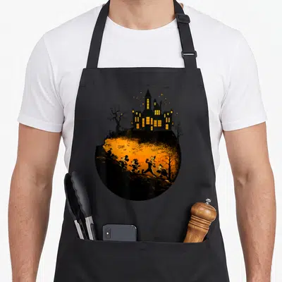 Halloween shot friends cooking apron - Circular haunted house with four characters running across orange landscape — shown on a black cotton canvas apron against a white background