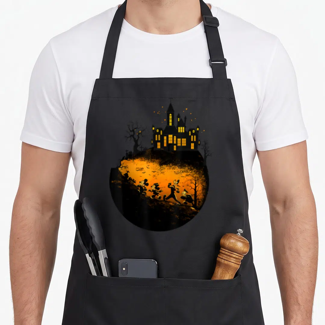 Halloween shot friends cooking apron - Circular haunted house with four characters running across orange landscape — shown on a black cotton canvas apron against a white background