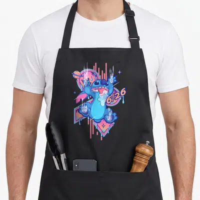 Drool stitch apron - Blue cartoon figure with 6/26 text, pink circle, orange drips, and hand prints — shown on a black cotton canvas apron against a white background