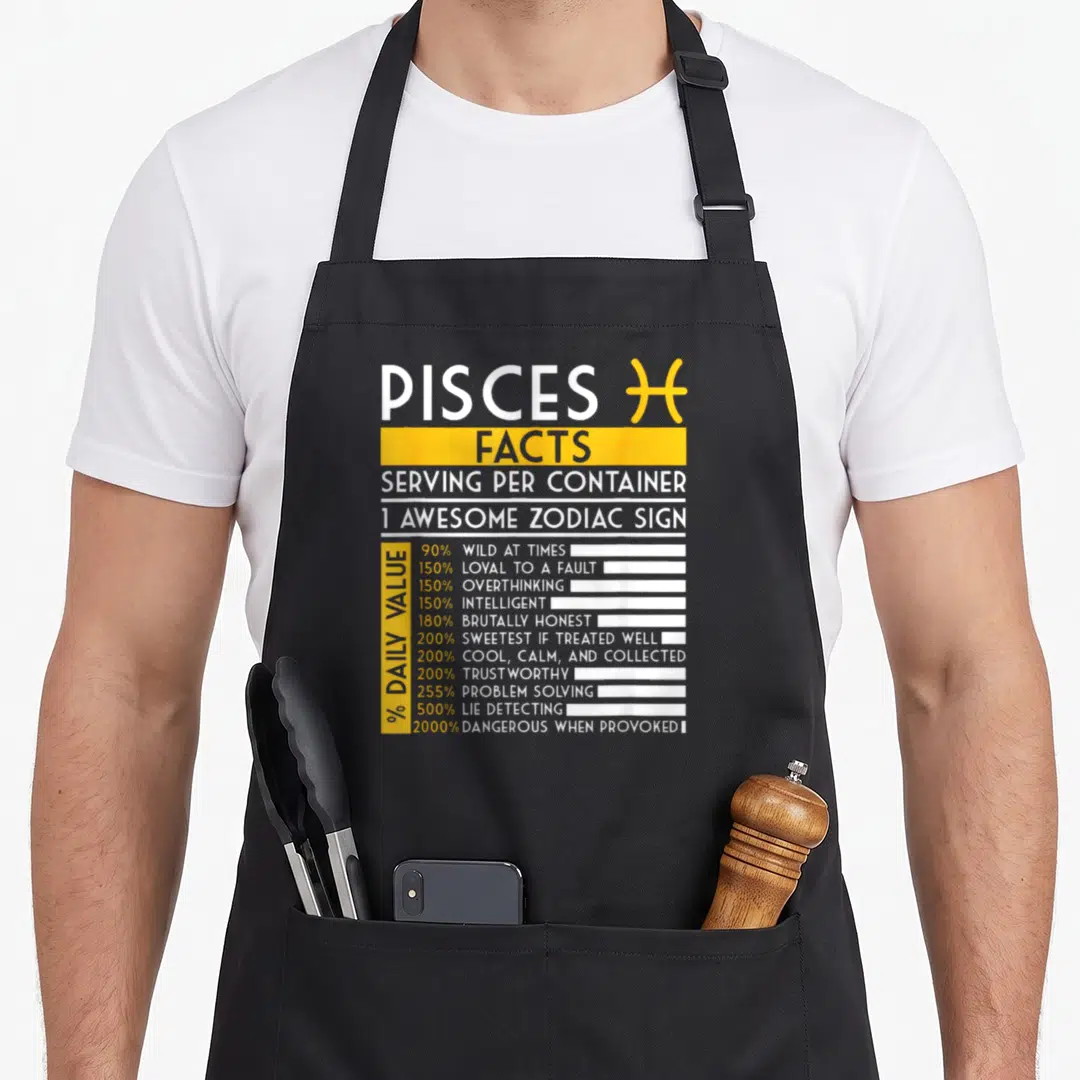 Pisce fact zodiac aprons - Nutrition facts style graphic listing Pisces traits like loyal and intelligent with yellow — shown on a black cotton canvas apron against a white background