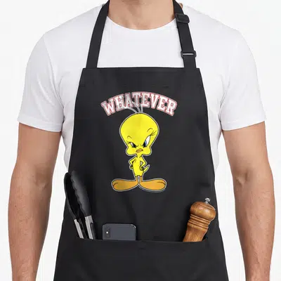 Tweety face apron - Arched WHATEVER text above a standing yellow cartoon bird with angry expression — shown on a black cotton canvas apron against a white background