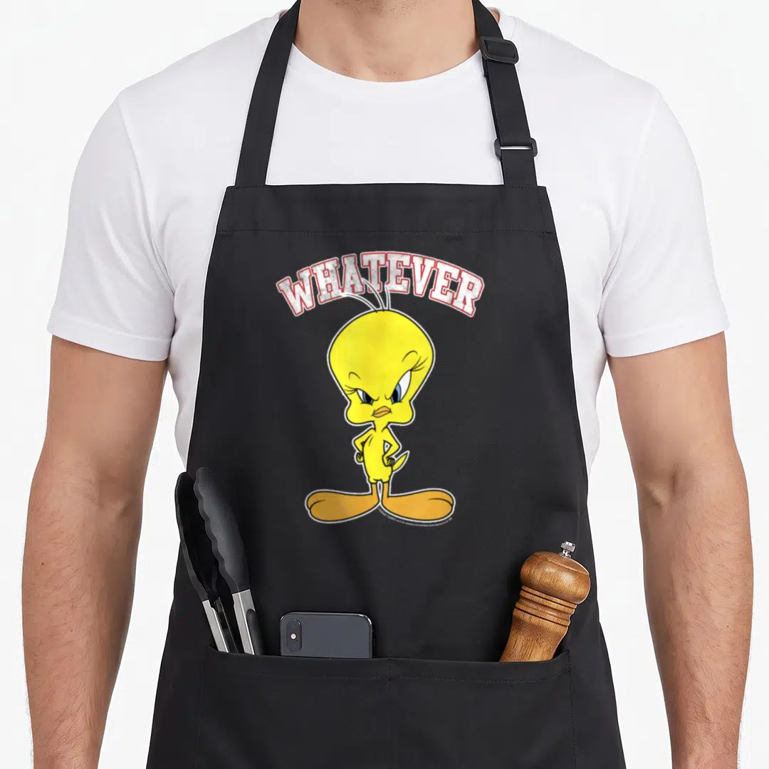 Tweety face apron - Arched WHATEVER text above a standing yellow cartoon bird with angry expression — shown on a black cotton canvas apron against a white background