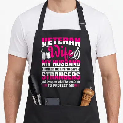 Soldier best husband apron - Pink and white distressed text reading Veteran Wife My Husband Risked His Life To Save — shown on a black cotton canvas apron against a white background