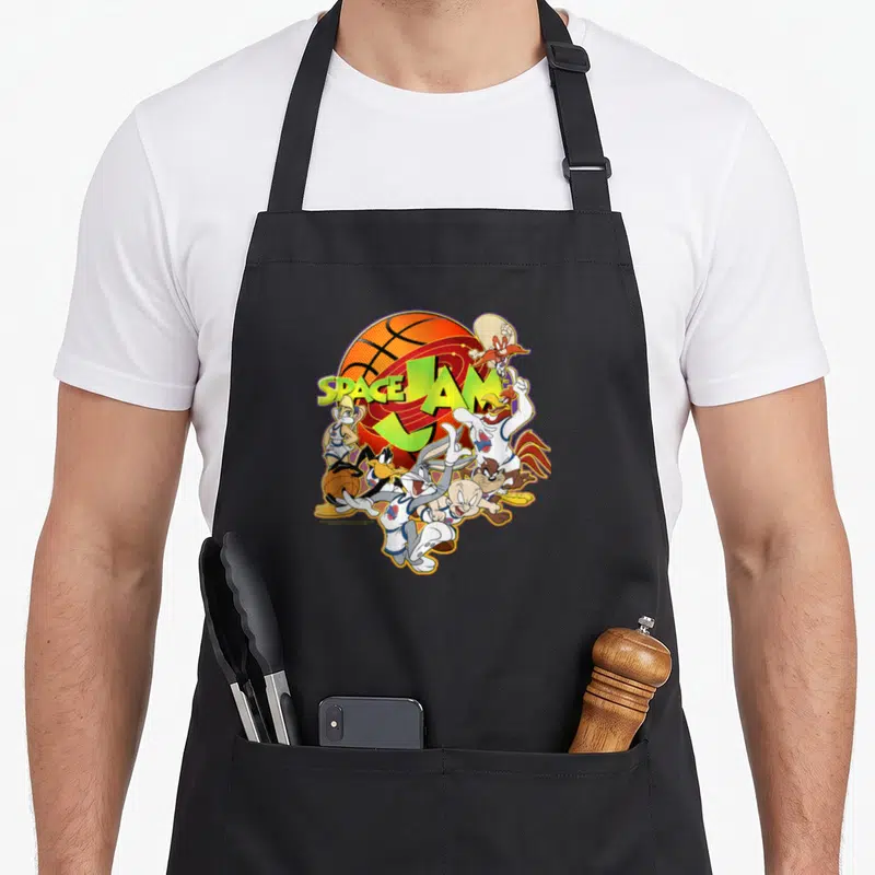 Funny space jam apron - Looney Tunes characters clustered around an orange basketball with centered SPACE JAM text — shown on a black cotton canvas apron against a white background