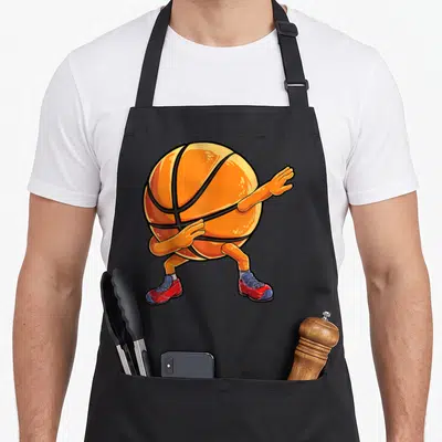 Dabbing point guard apron - Cartoon orange basketball with arms legs and red blue sneakers in a dab pose — shown on a black cotton canvas apron against a white background
