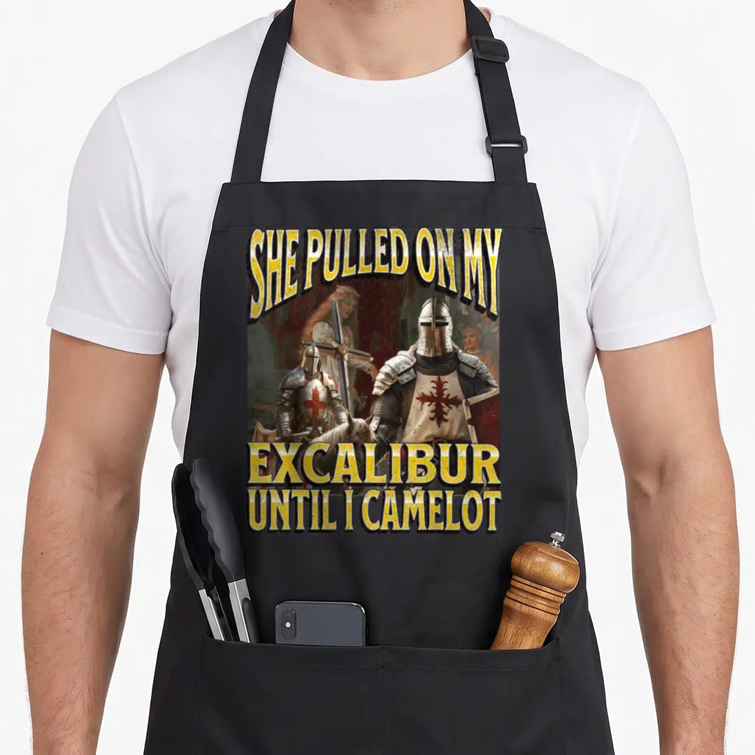 Pulled meme apron - Distressed knight art with yellow text She Pulled On My Excalibur Until I Camelot — shown on a black cotton canvas apron against a white background