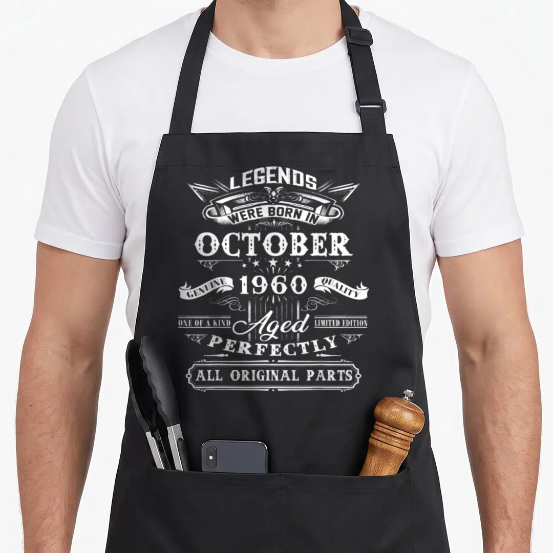 October 60th birthday apron - White distressed text legends born October 1960 on black apron — shown on a black cotton canvas apron against a white background