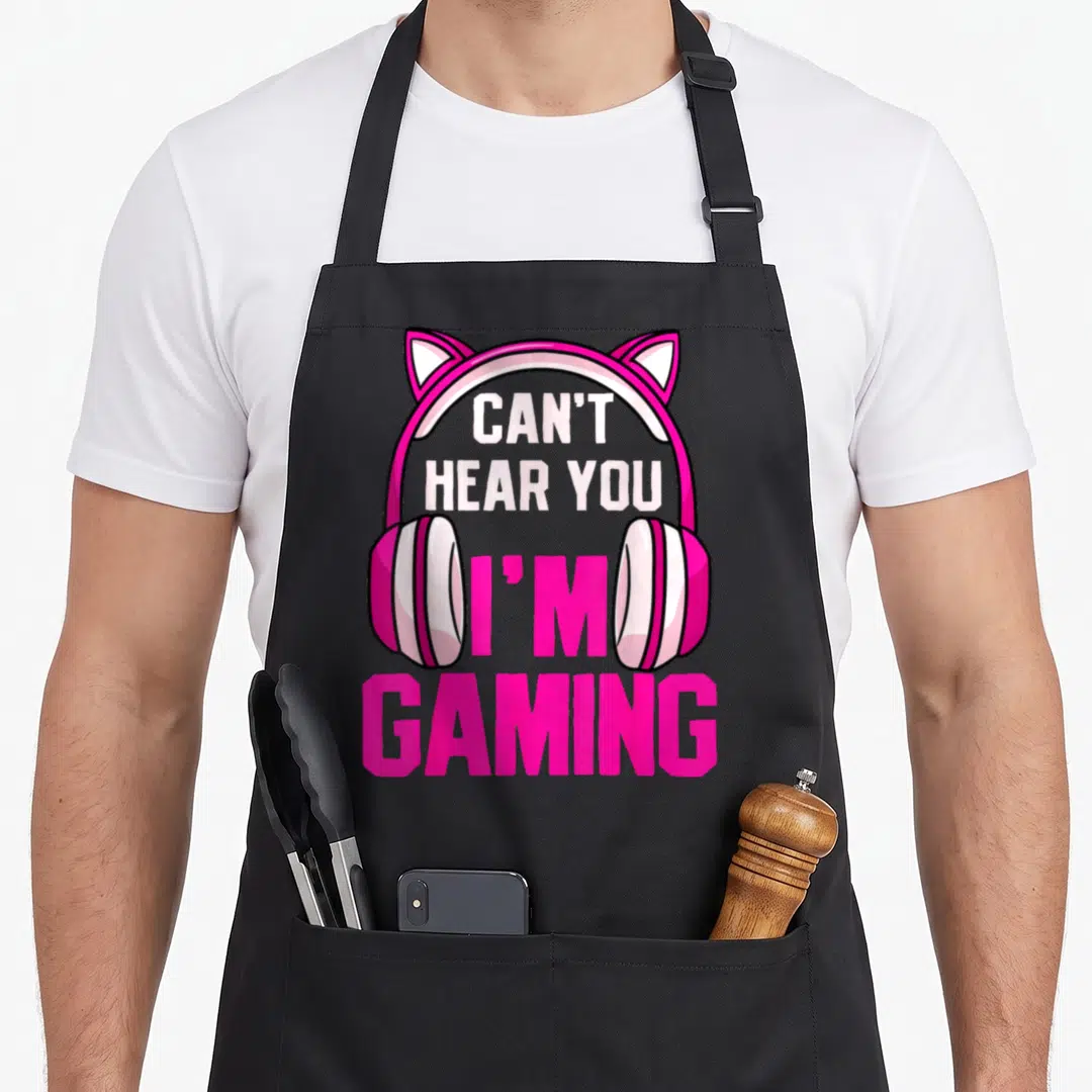 Hear video game apron - Pink cat-ear headphones with text CAN'T HEAR YOU I'M GAMING in white and pink — shown on a black cotton canvas apron against a white background