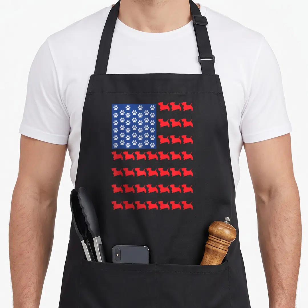 Scottish terrier 4th of july apron - Stylized flag with white paw prints on blue field and red rows of dog silhouettes — shown on a black cotton canvas apron against a white background