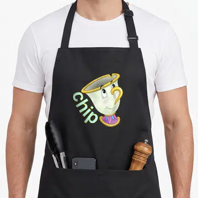 Chip face apron - Cartoon teacup with gold rim and blue text reading Chip — shown on a black cotton canvas apron against a white background