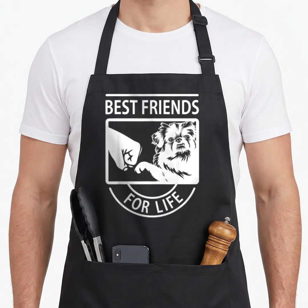 Pekingese friends apron - White line art of Pekingese dog fist-bumping human hand with text Best Friends For Life — shown on a black cotton canvas apron against a white background